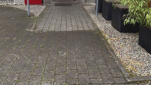 Ein Gebäudeeingang mit roter Markise, einer Holztür und einem befestigten Weg, der dorthin führt.