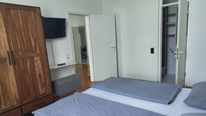 Ein Schlafzimmer mit zwei Betten, einem Kleiderschrank, einem Fernseher und einer Badezimmertür.