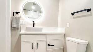A bathroom with a white sink, a round mirror, a toilet, and a towel rack. - Exotic home Rogers by sdstay (Casa de Oro-Mount Helix)