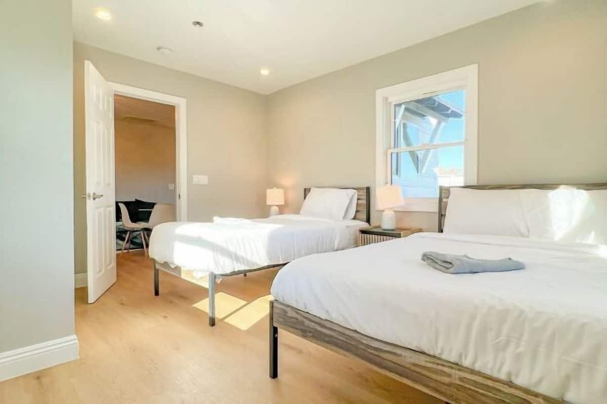 A bedroom with two beds, a window, and a door leading to another room.