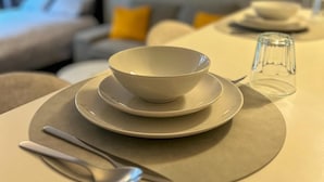 Ein ordentlich gedeckter Esstisch mit Schüssel und Löffel, einem Glas und einem Bett im Hintergrund.