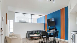 A modern living room with a sofa, a dining table with chairs, a TV mounted on the wall, and a kitchen area with a stove. - Olde City Loft Style Condo (Philadelphia)