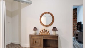 A room with a wooden dresser, a round mirror, two lamps, and a brick wall in the background. - Olde City Loft Style Condo (Philadelphia)