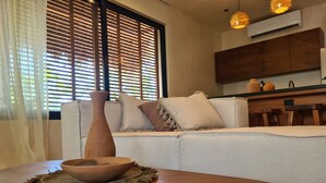 Un salón moderno con una mesa de madera, un sofá blanco y un amplio ventanal con persianas.