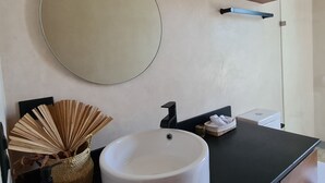 Un baño con un espejo redondo, un lavamanos blanco, una encimera negra y un estante de madera sobre el espejo.