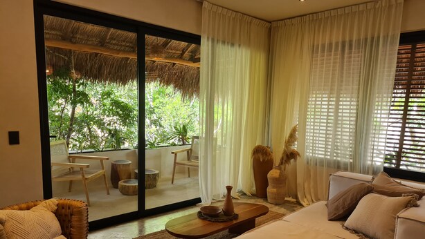 Amplia sala de estar con un gran ventanal corredizo que da a un patio exterior, amoblada con un sofá, sillones y una mesa de centro.