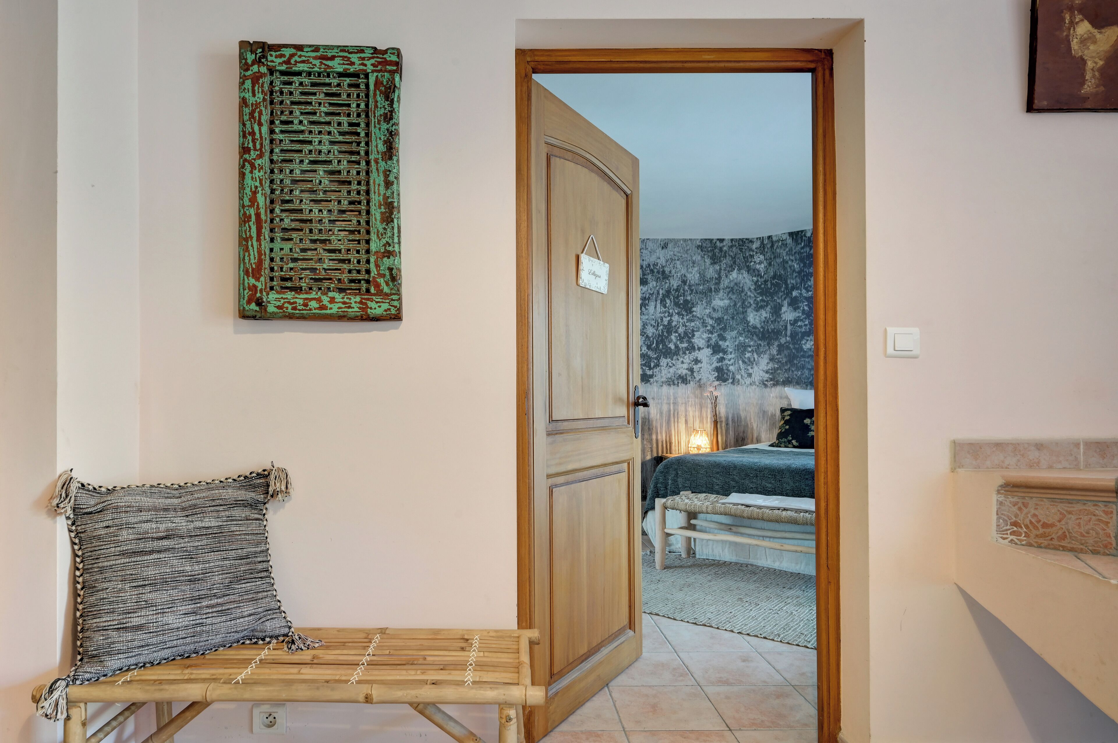 Una habitació amb una cadira de fusta, una porta que condueix a una altra estança i una paret amb una obra d'art amb textura.