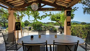 An outdoor patio with a round table and chairs, surrounded by greenery and a view of the countryside. - La Villa Kef (Mallemort)