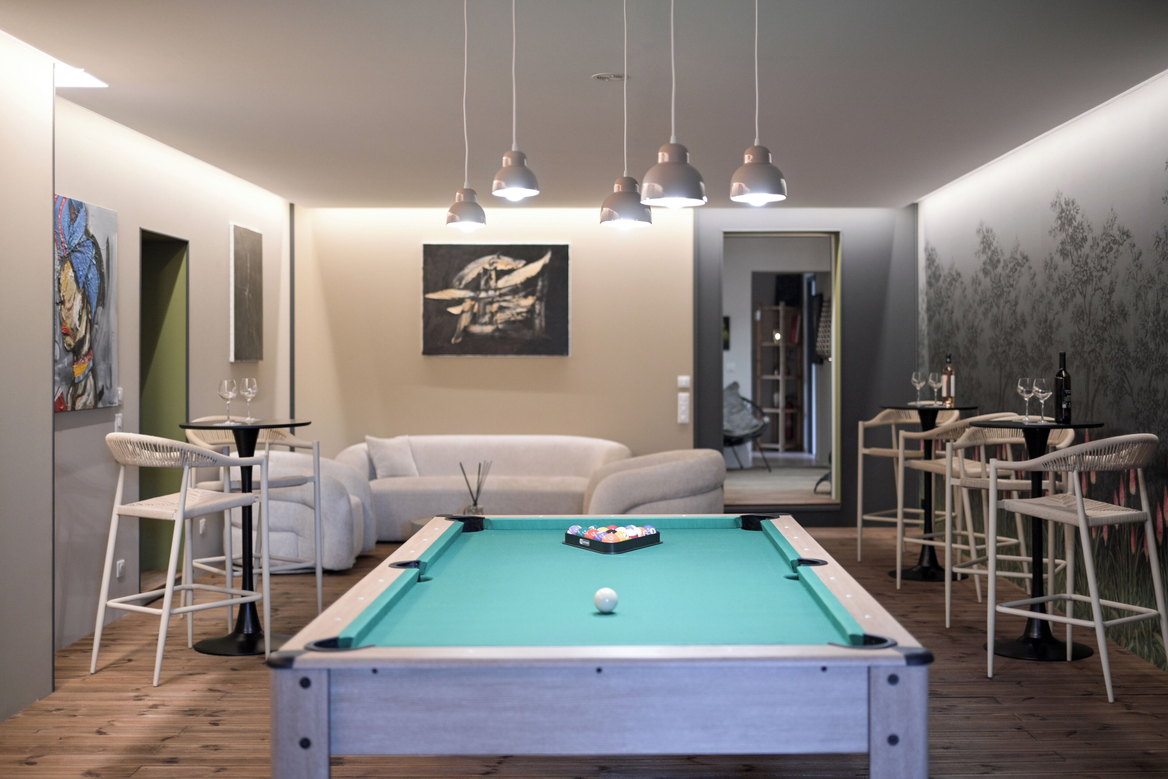 Ein Billardtisch in einem Raum mit einer Couch, Sesseln und Kunstwerken an den Wänden.