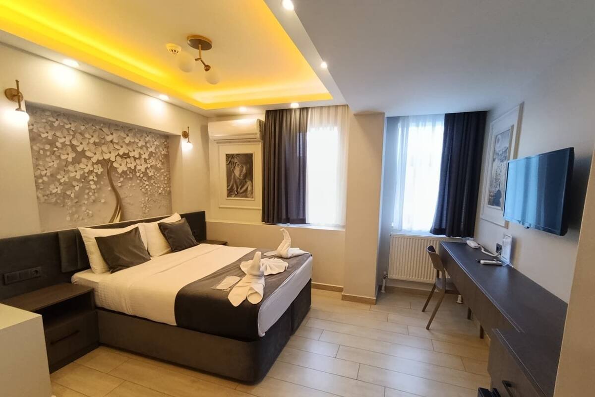 Una habitación de hotel moderna con una cama grande, mesitas de noche, un escritorio y un televisor.