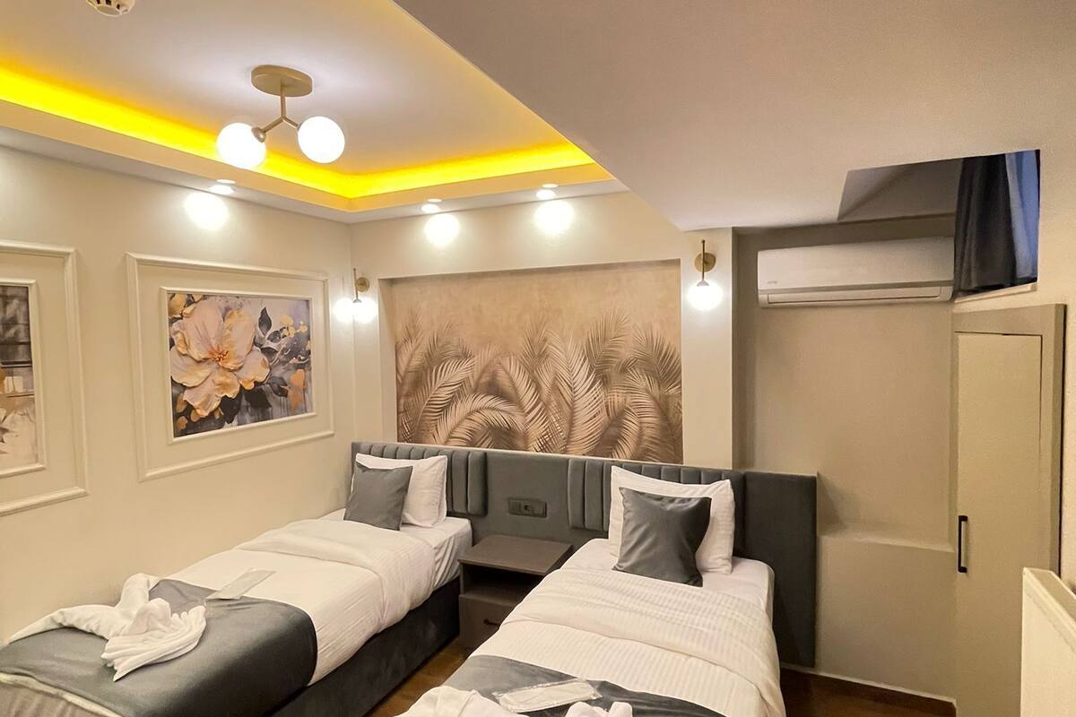 Habitación de hotel con dos camas, un mural grande en la pared, una lámpara en el techo y un equipo de aire acondicionado.