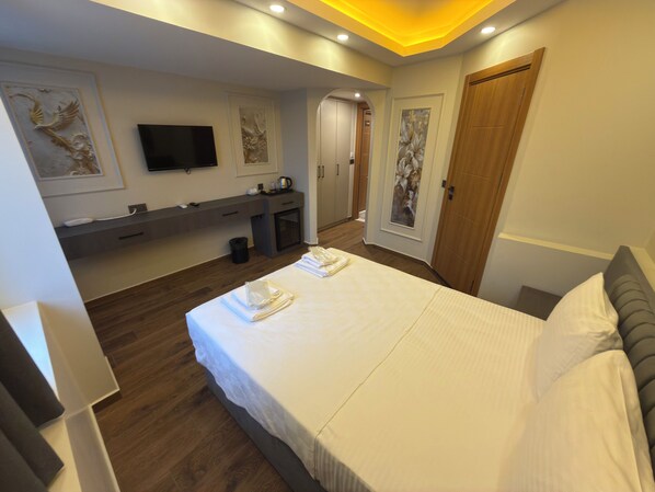 A modern hotel room with a large bed, a vanity with a mirror, a flat-screen TV, and a door leading to a bathroom.