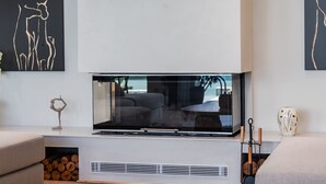 A modern living room with a large flat-screen TV mounted on a white console, a sofa, a decorative vase, and a fireplace. - Horizon Villa Luxurious Lakefront Retreat (Shkodër)