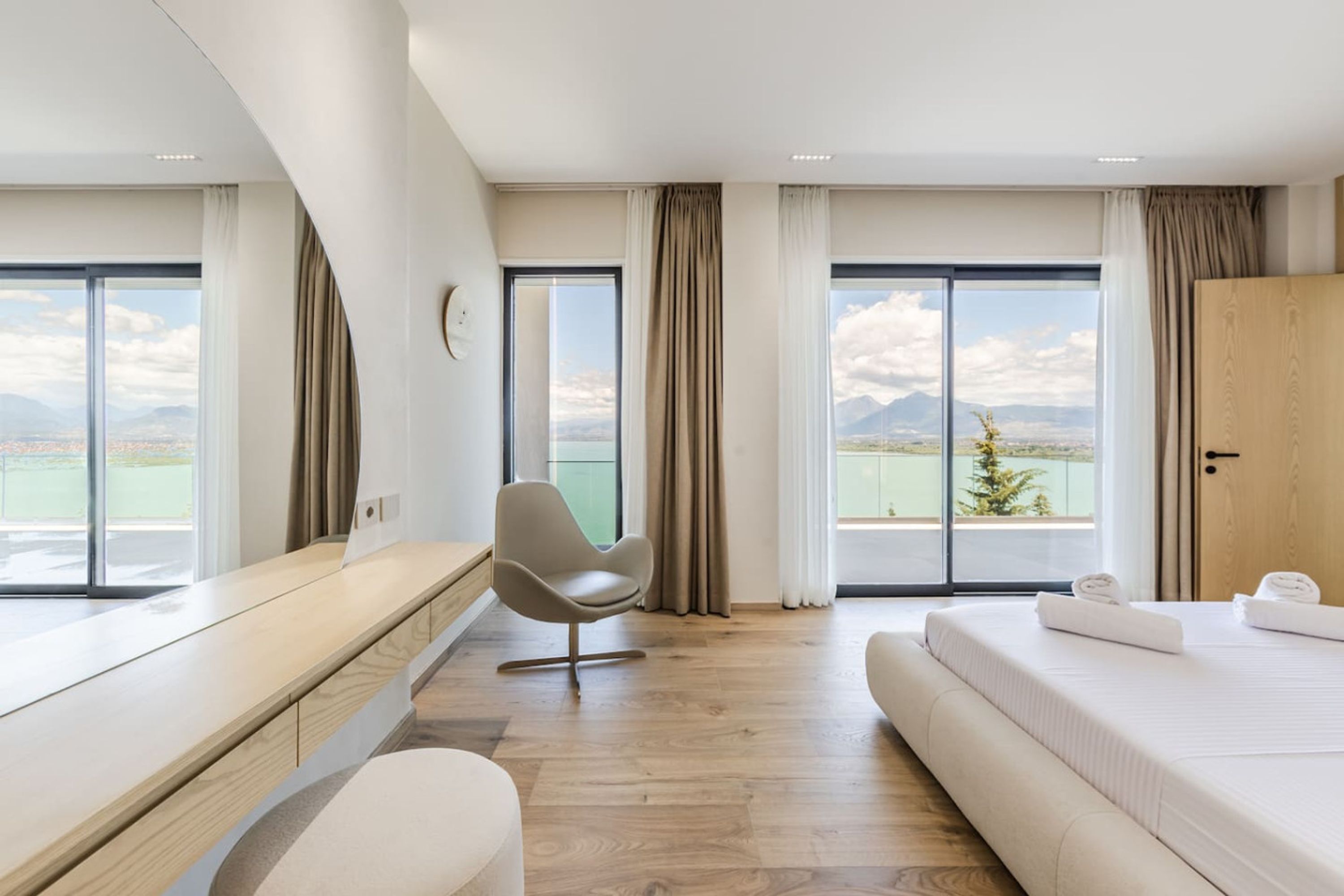 A modern hotel room with a large bed, a desk, a chair, and a view of the mountains.