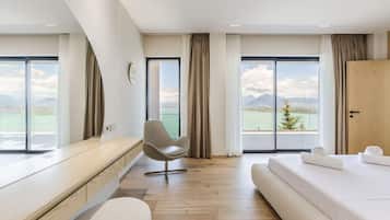 A modern hotel room with a large bed, a desk, a chair, and a view of the mountains.
