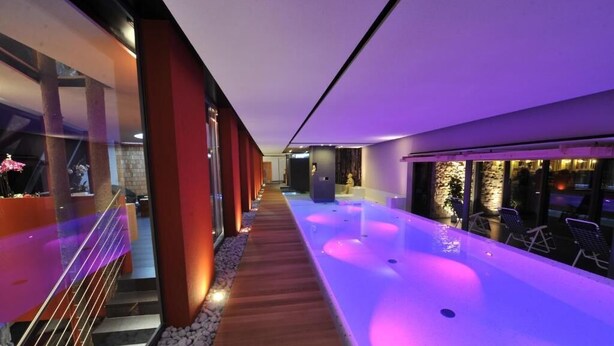 Un área de piscina interior moderna con una terraza de madera y una piscina larga y estrecha.