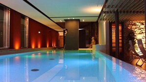 Una piscina interior moderna con superficie de agua cristalina, rodeada de paredes rojas y una pérgola de madera.
