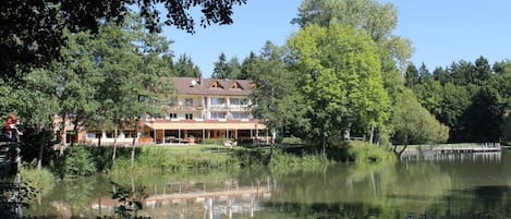 Hotel na beira do lago com um edifício grande, refletido na água, rodeado de árvores.