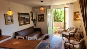 Ein gemütliches Wohnzimmer mit einer Couch, einem Holztisch und Korbstühlen. An den Wänden befinden sich gerahmte Bilder und eine Pendelleuchte.