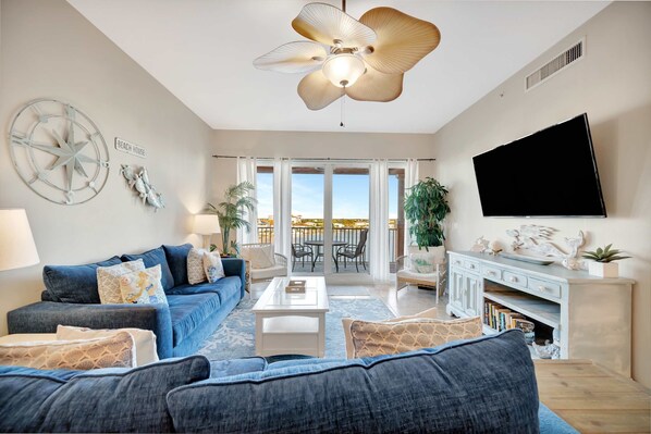 Ein Wohnzimmer mit einer großen Couch, einem Couchtisch, einem Fernseher und einem Balkon mit Blick.