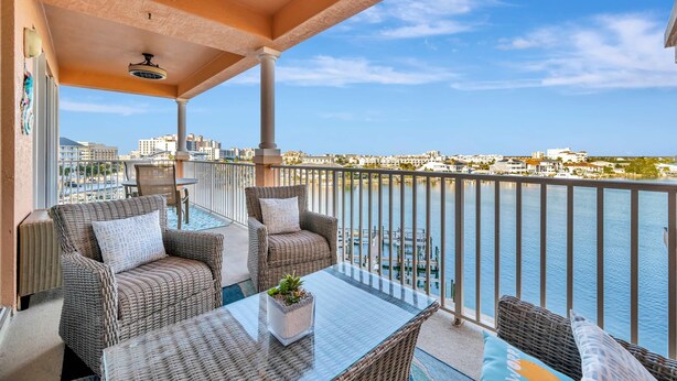 A balcony with wicker furniture, a glass table, and a view of the water and cityscape. - Waterfront 3B Balcony Hot Tub Pool Near Beach (Clearwater Beach)