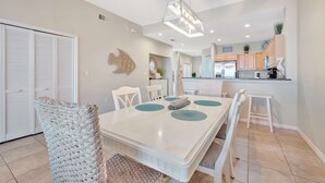 A dining area with a white table, chairs, and a hanging light fixture. - Waterfront 3B Balcony Hot Tub Pool Near Beach (Clearwater Beach)