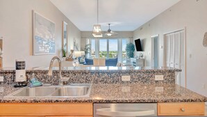 A kitchen with granite countertops, a stainless steel sink, and a ceiling fan. - Waterfront 3B Balcony Hot Tub Pool Near Beach (Clearwater Beach)