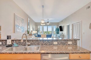 A kitchen with granite countertops, a stainless steel sink, and a ceiling fan. - Waterfront 3B Balcony Hot Tub Pool Near Beach (Clearwater Beach)