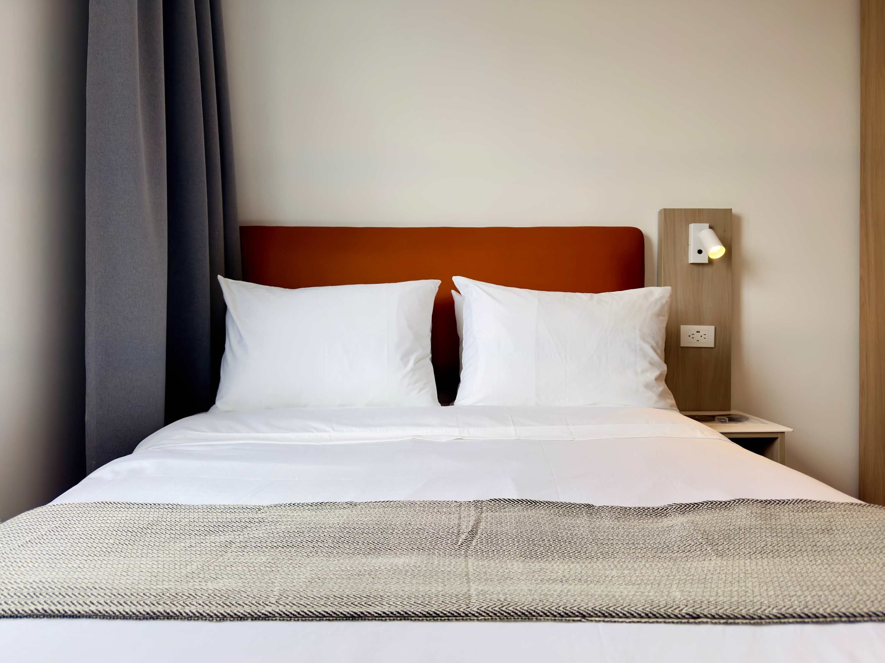 A neatly made bed with white linens and a grey and black patterned throw.