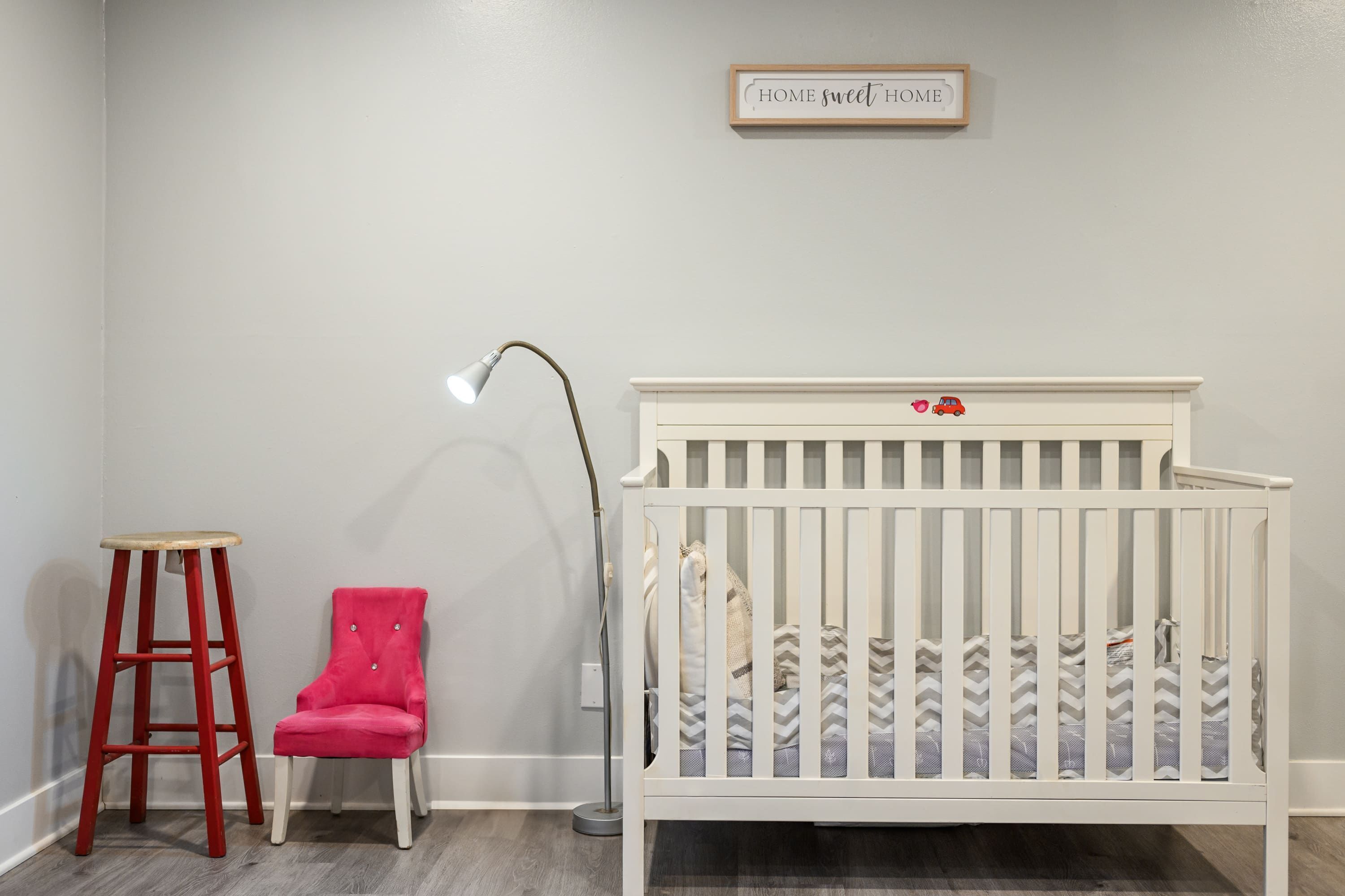 A white crib with a chevron-patterned mattress and a small red toy car on the headboard.