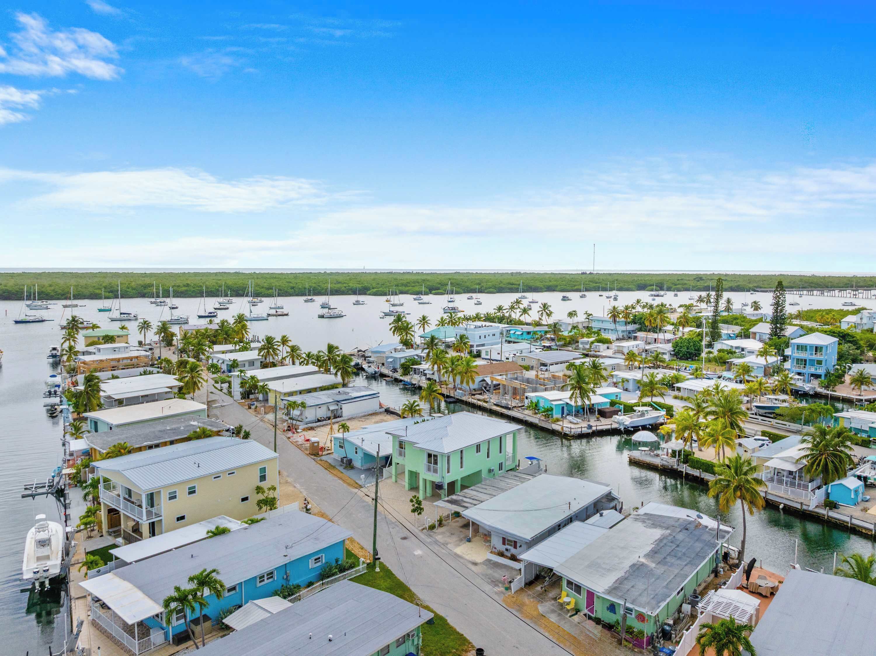 A marina with multiple boats docked, surrounded by residential buildings and palm trees.