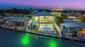 Une maison à deux étages avec une piscine, entourée d’une clôture et située près d’une étendue d’eau.
