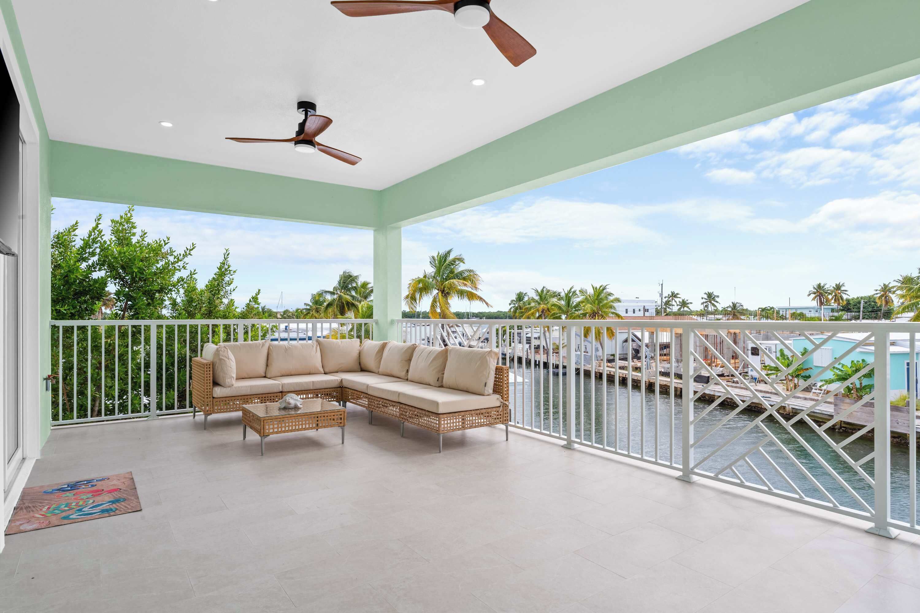A balcony with a wicker sofa, a small table, and a ceiling fan.