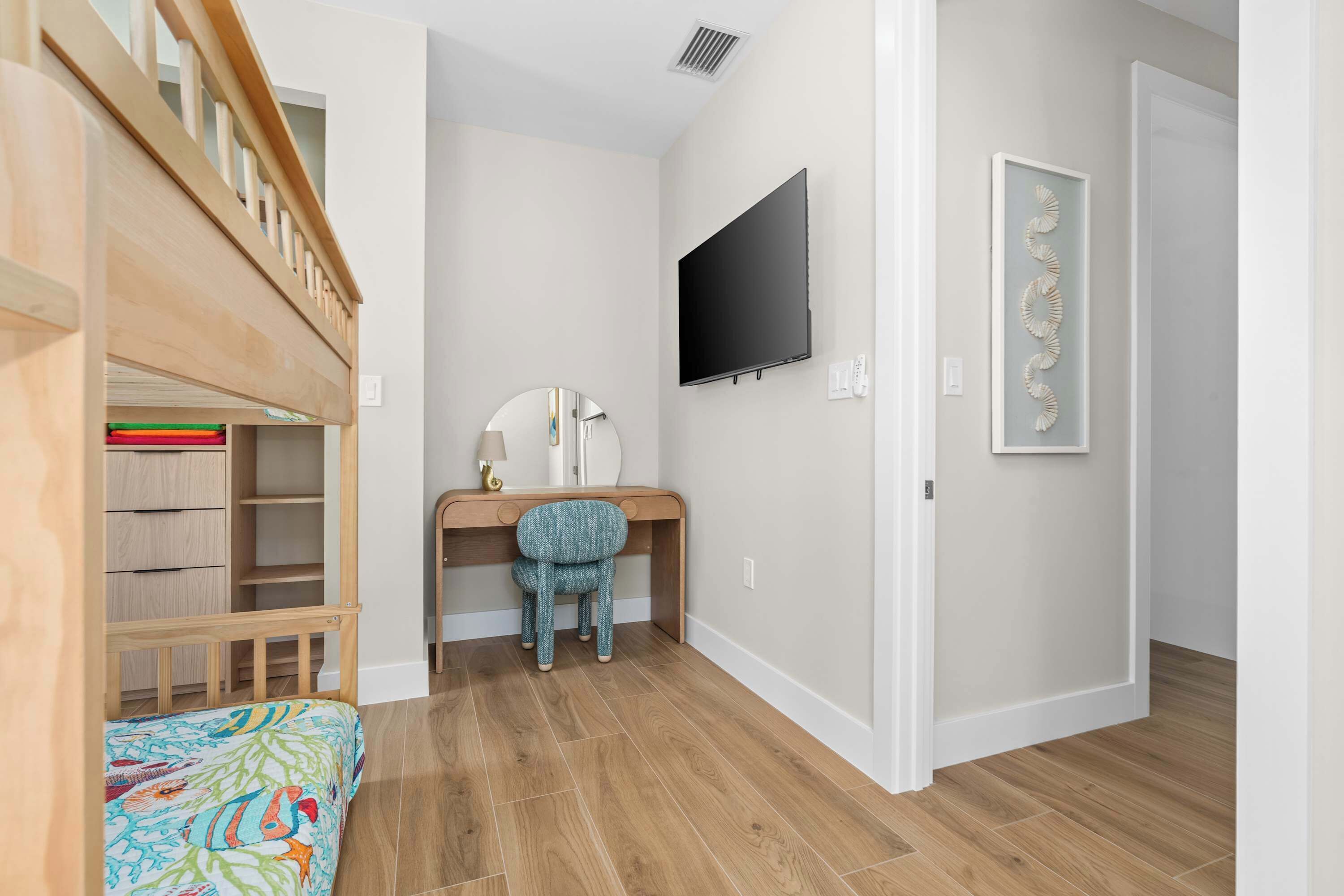A child's bedroom with a bunk bed, desk, chair, and a TV mounted on the wall.