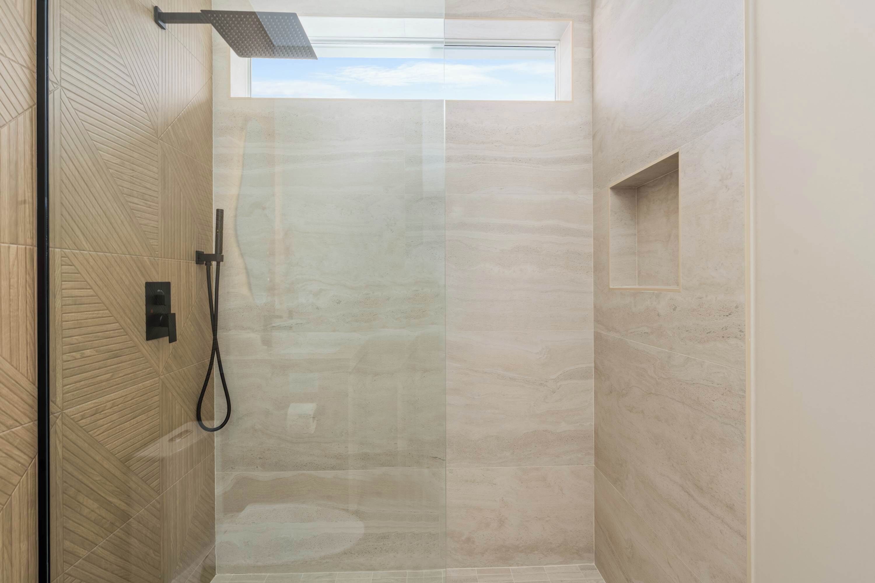 Ducha moderna con puerta de vidrio, repisa integrada y tragaluz.