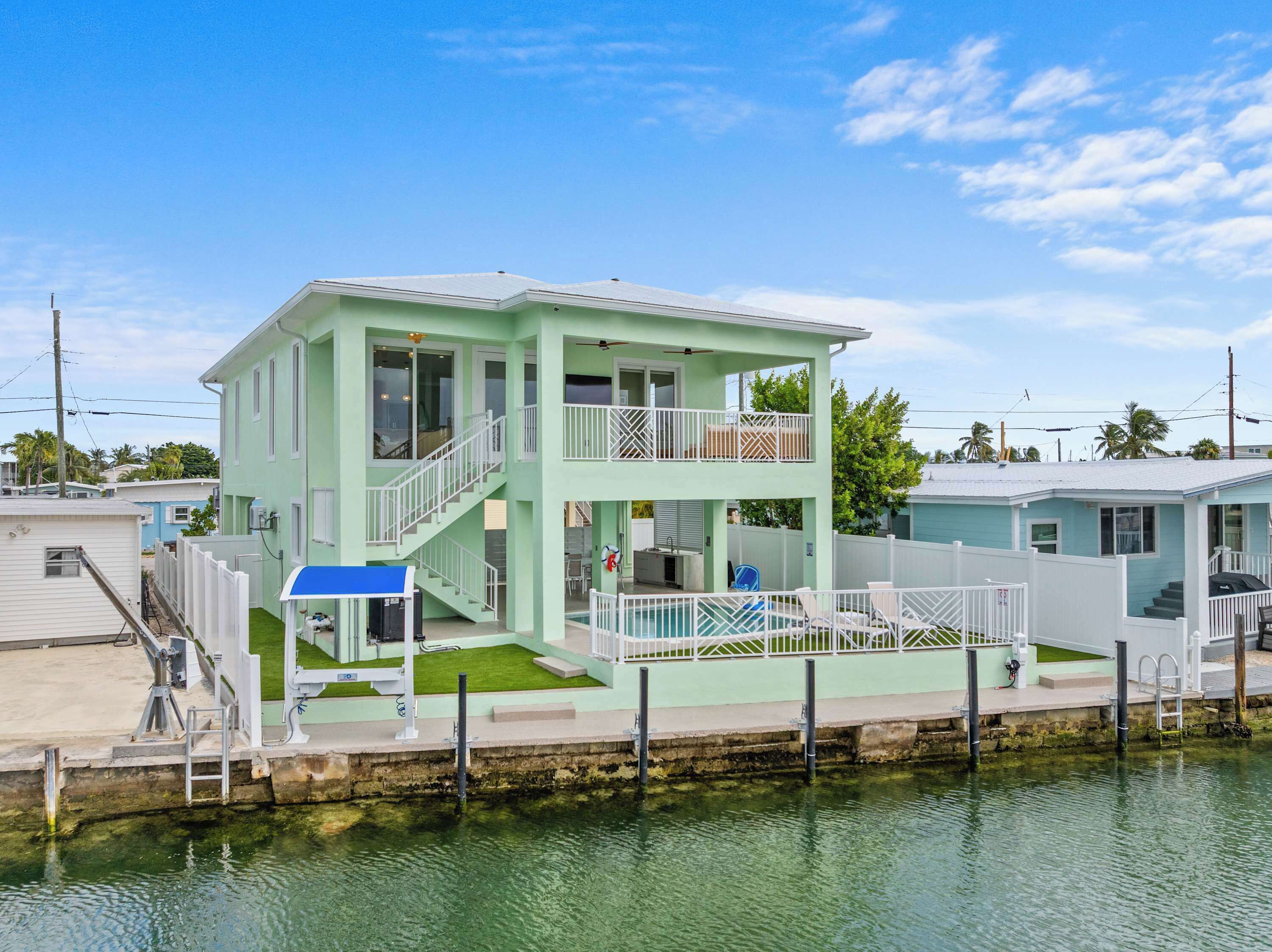 Une maison à deux étages dotée d’un balcon, d’une piscine et d’une jetée qui s’avance dans l’eau.