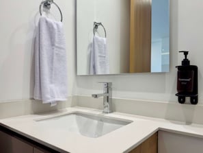 Een badkamer met een witte wastafel, een spiegel en een handdoekrek met twee handdoeken.