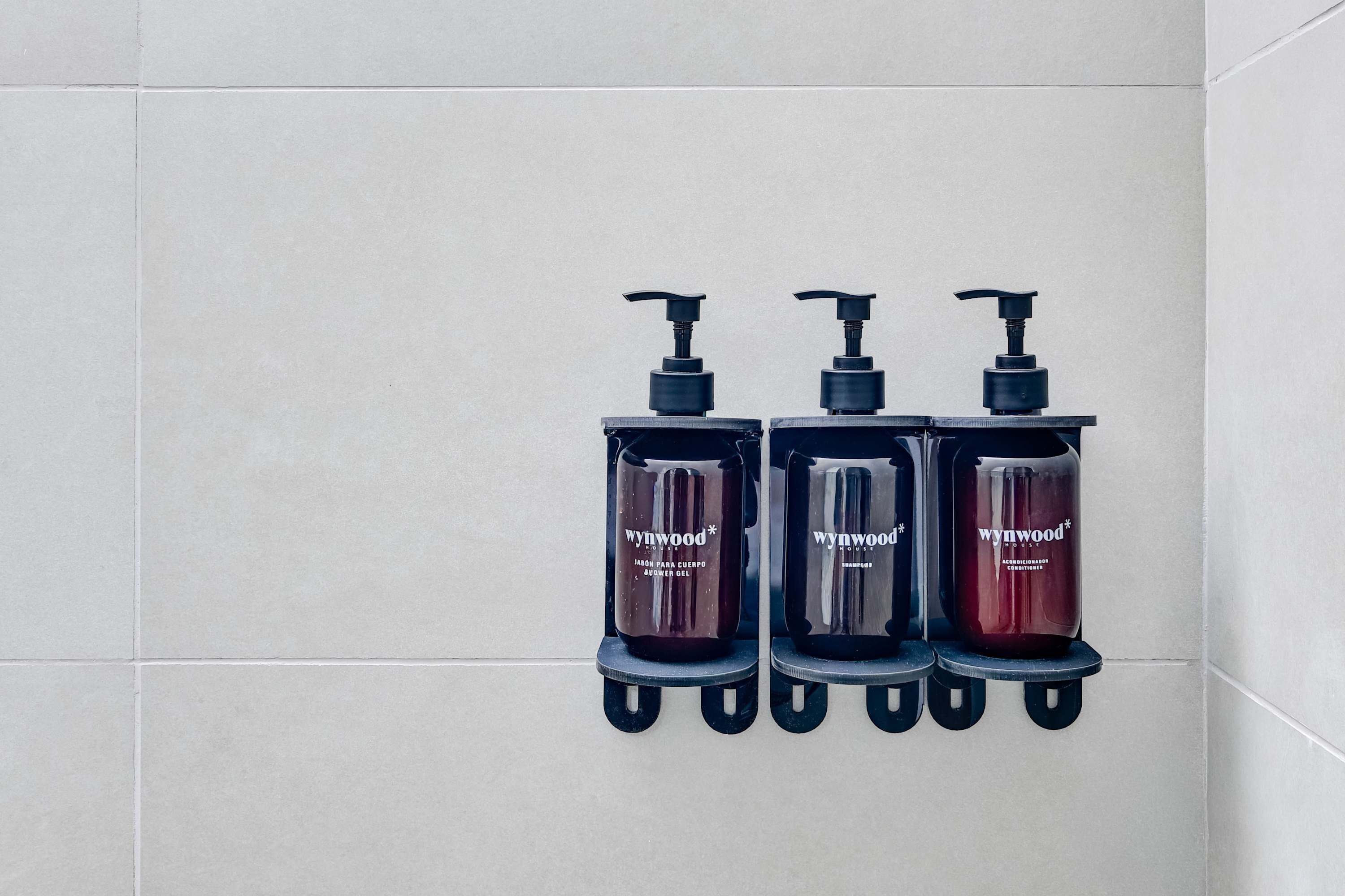 Tres dispensadores negros con bombas en una pared de azulejos.