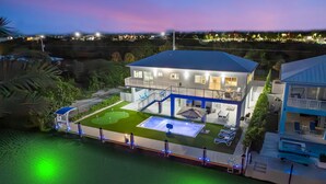 Una casa de dos pisos con piscina, mobiliario exterior y vista al océano.