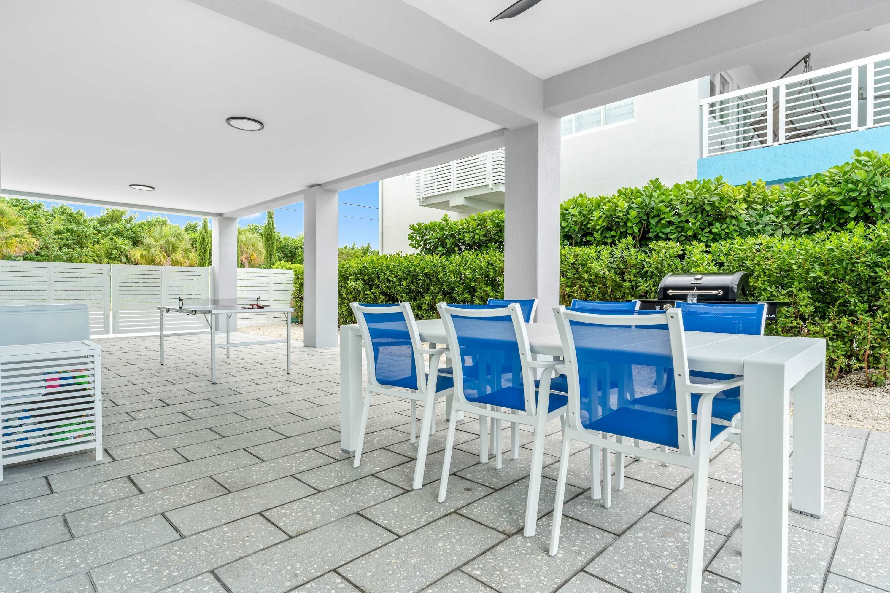 An outdoor patio area with white and blue chairs, a table, and a grill.