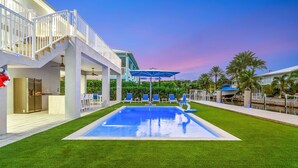 Una casa moderna con piscina, mobiliario exterior y una escalera que lleva a un balcón.