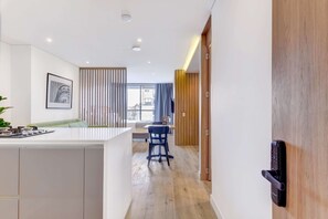 A modern kitchen with a central island, a dining area with a blue chair, and a view of the city through large windows. - w Heavenly Loft w Balcony in Santa Barbara (Bogotá)