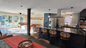 Una cocina moderna con una isla central, asientos tipo bar y un comedor con camino de mesa rojo.
