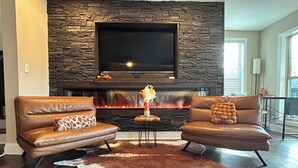Una sala de estar con sofás de cuero, una chimenea de piedra, un televisor de pantalla plana y un tapete de piel de vaca.