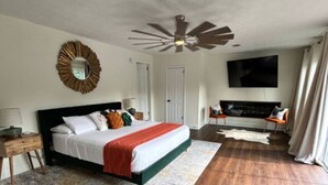 Un dormitorio espacioso con una cama grande, ventilador de techo, televisor de pantalla plana y chimenea.