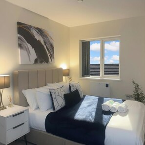 Een moderne hotelkamer met een groot bed, een nachtkastje, een bedlampje, een raam met uitzicht op de lucht en een schilderij aan de muur.