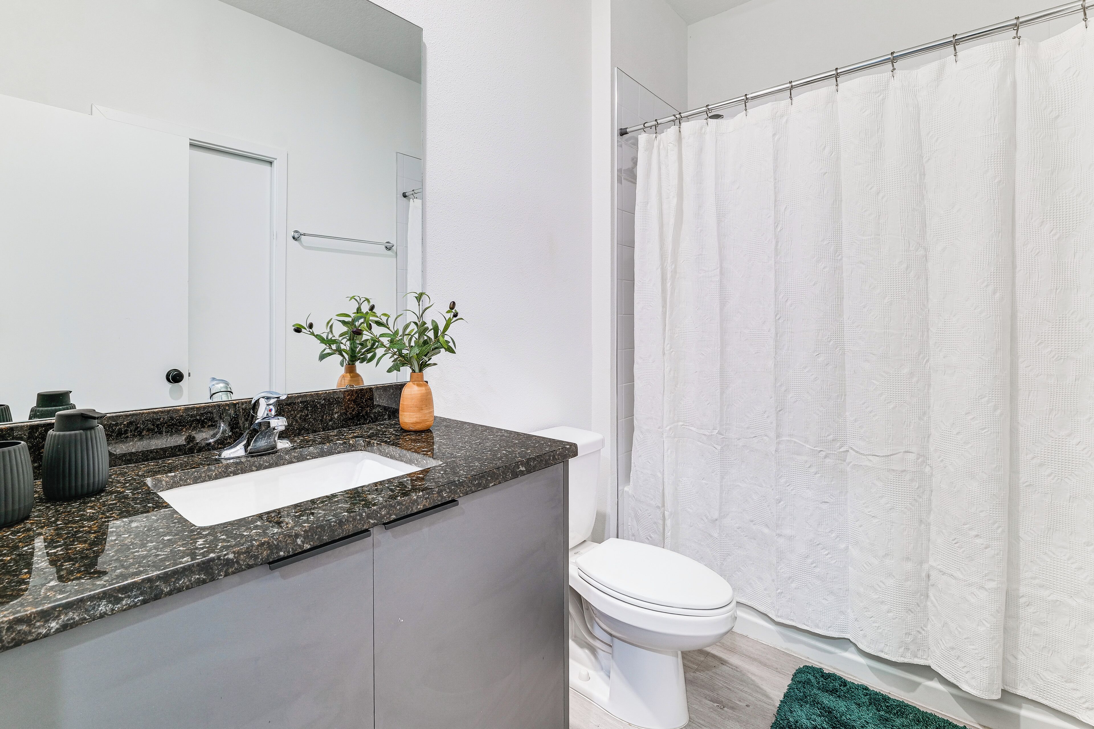 A bathroom with a granite countertop sink, a white toilet, and a shower curtain.