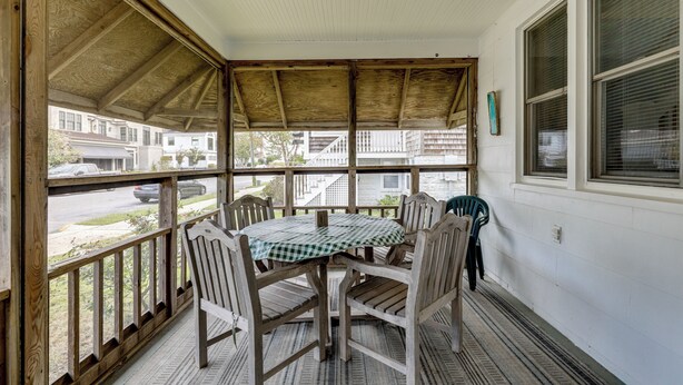 Une véranda avec une table et des chaises, des balustrades en bois et de grandes fenêtres.
