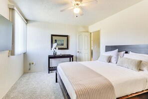 A bedroom with a large bed, a ceiling fan, a nightstand, and a framed picture on the wall.