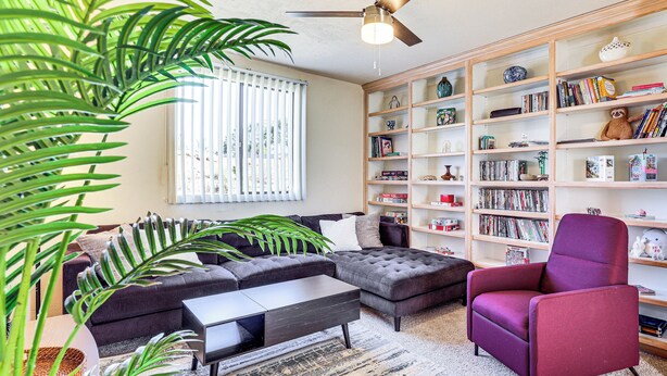 A living room with a sectional sofa, a coffee table, a purple armchair, and a bookshelf filled with books and decorative items.